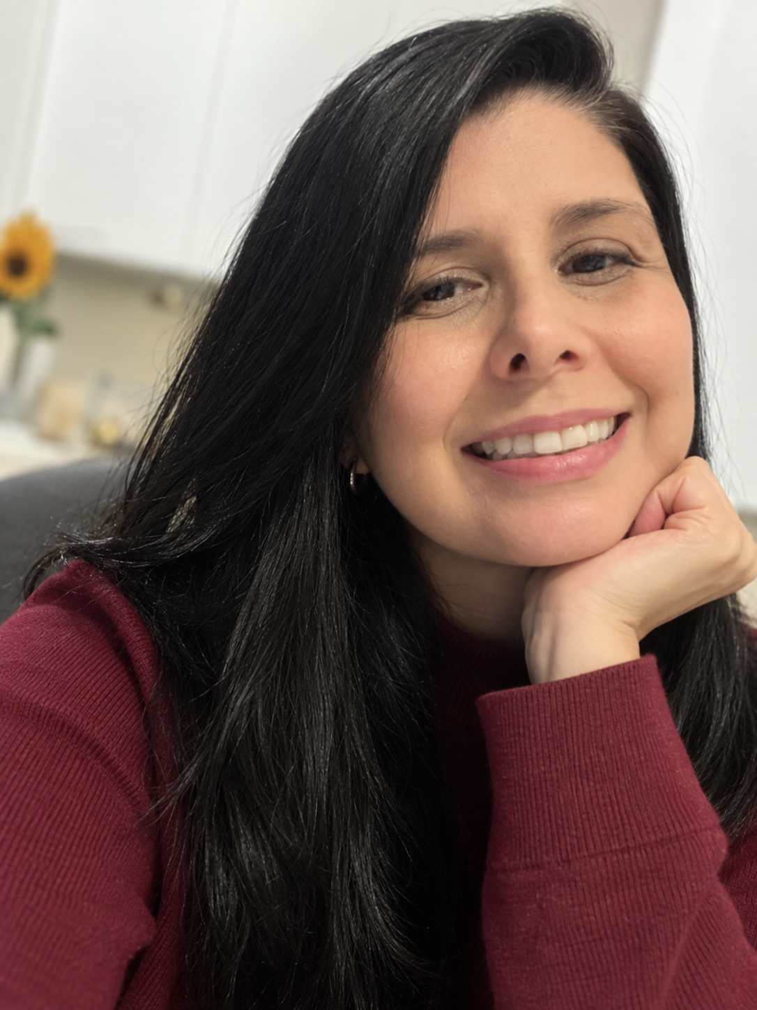 Yuribeth Molina smiling, wearing a burgundy sweater with her hand resting on her face